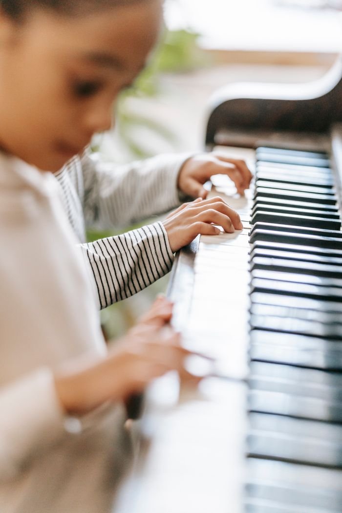 Side view of crop unrecognizable ethnic kids playing piano together in light room