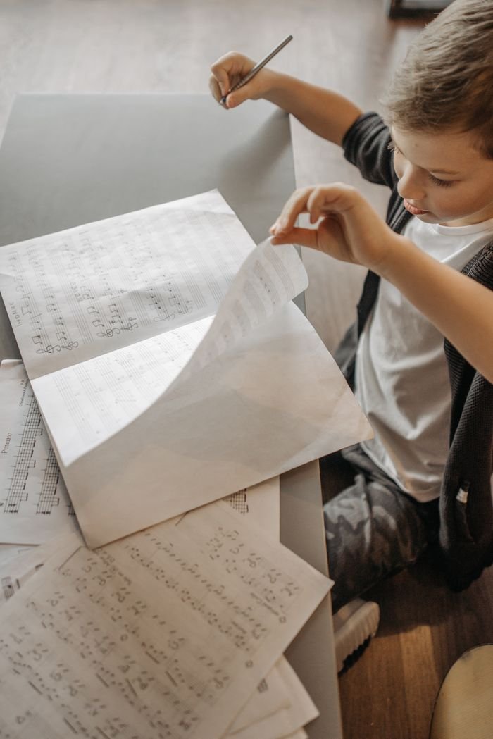 Boy concentrates on studying musical notes at a desk indoors, fostering learning and creativity.