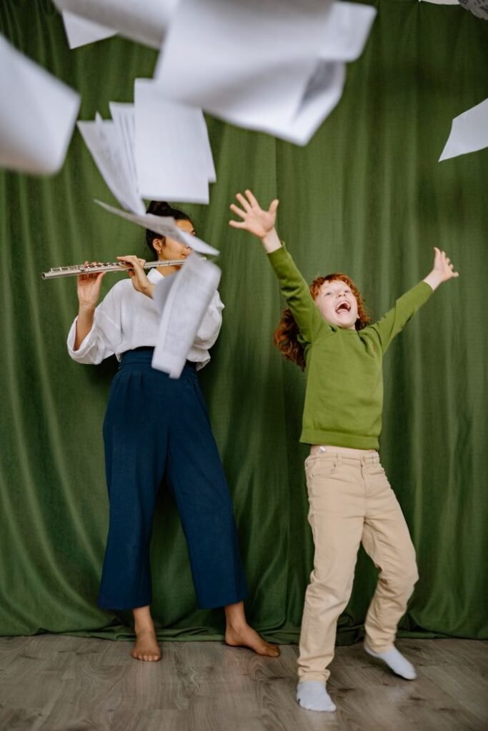A cheerful child dances as a woman plays the flute, with papers flying around in a lively music lesson.