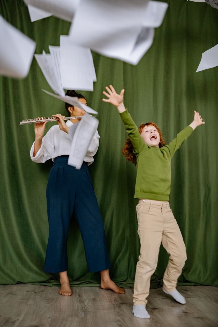 Crafting Captivating Headlines: Your awesome post title goes here A cheerful child dances as a woman plays the flute, with papers flying around in a lively music lesson.