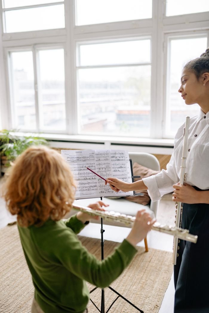 A young boy learns to play the flute under the guidance of an instructor indoors.