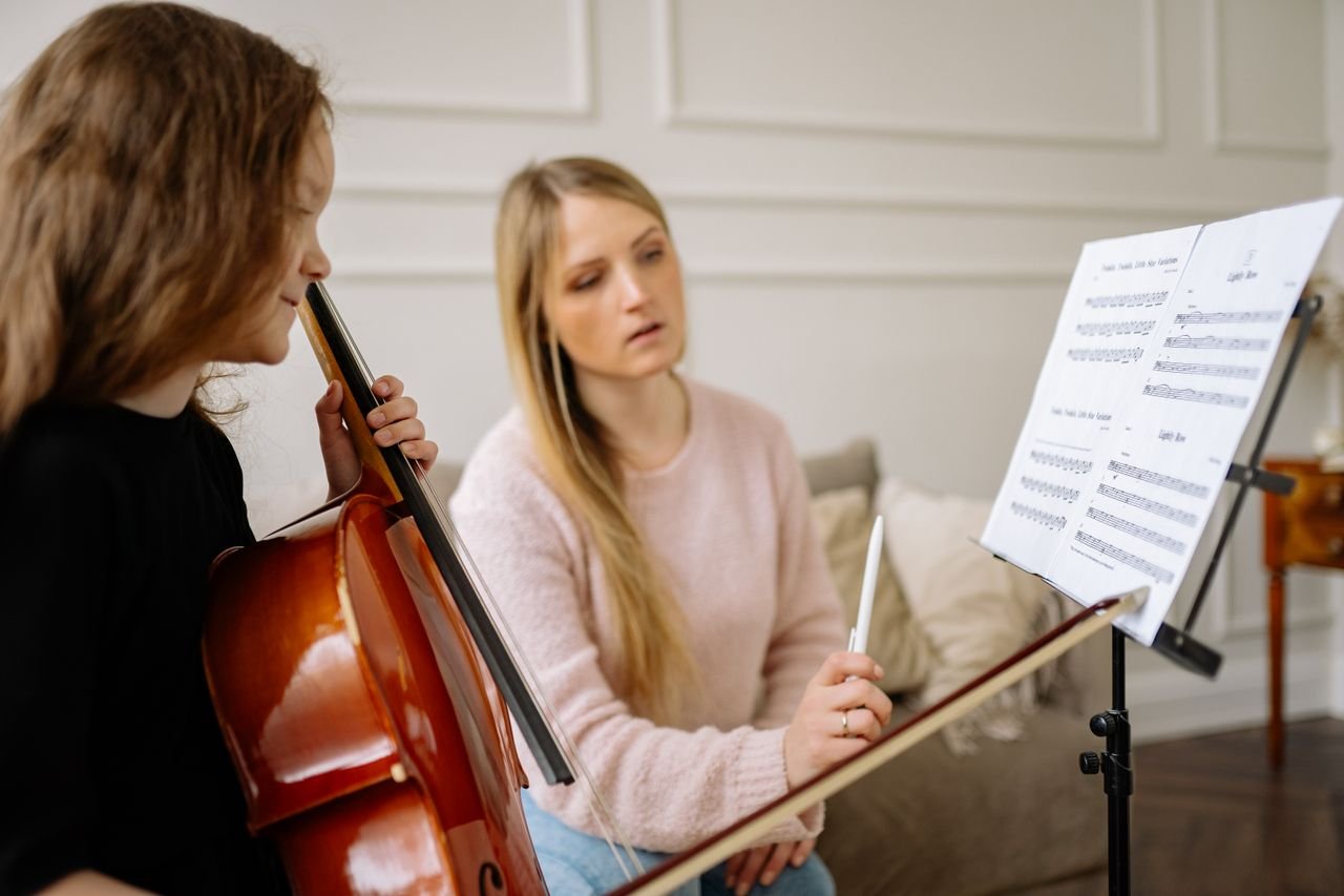 A music lesson featuring a child learning to play the cello, guided by a female teacher.